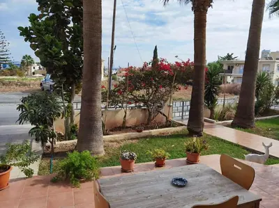 a wooden table sitting on a patio with palm trees at Lovely house apartment Oroklini in Voroklini