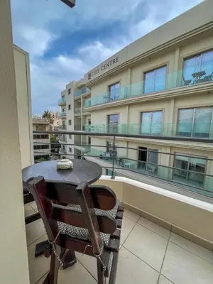 a table and chair on a balcony with a building at DownTown Studios & Two-Bedrooms in Larnaka