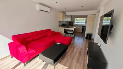 a red couch in a living room with a kitchen at Modern 1-bedroom home in Larnaca with a private garden ideal for long stays and remote work in Larnaka