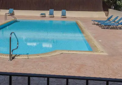 a swimming pool with two lawn chairs and two chairs at Napiana Apartments in Ayia Napa