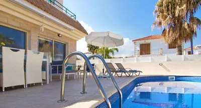 a swimming pool with an umbrella next to a house at Sonja in Paralimni