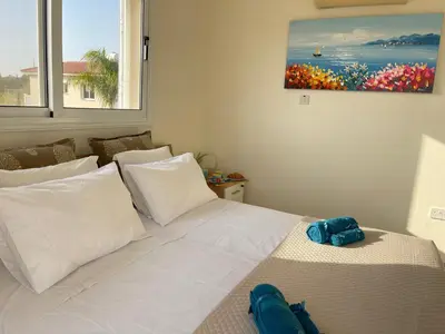 a bedroom with a white bed and a painting on the wall at Star Apt in front Nissi whit Sea View in Ayia Napa