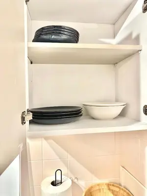 a white kitchen with plates and bowls on shelves at Sea and Lake Breeze 1BR Apt in Larnaka