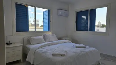 a white bedroom with a bed and two windows at STAY Chrisoula Beach Garden in Voroklini