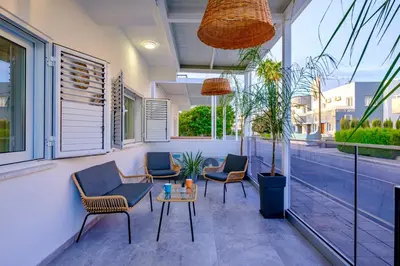 a patio with chairs and a table and windows at FatCow Beach Apartment in Larnaka