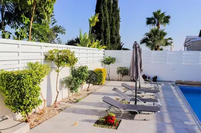 a patio with lounge chairs and an umbrella next to a pool at Marios Villa in Larnaka
