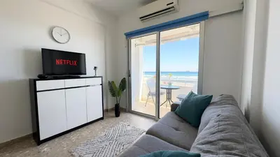 a living room with a couch and a tv and a balcony at Kolonaki Seaview 1BDR Finikoudes in Larnaka