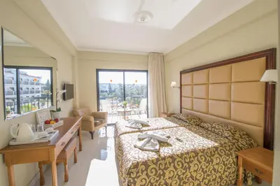 a hotel room with a bed and a desk and a room at Tsokkos Gardens Hotel in Protaras