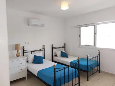 a bedroom with two beds with blue sheets and a window at Nissi Retreat - Walk to Nissi beach! in Ayia Napa