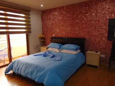 a bedroom with a bed with blue sheets and a red wall at Ithaki Phinikoudes Apartment No. 207 in Larnaka
