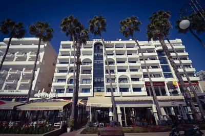 a white building with palm trees in front of it at Krasas Beach Apartment Rentals in Larnaka