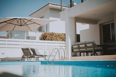 a swimming pool with two chairs and an umbrella at Jupiter Villa in Voroklini