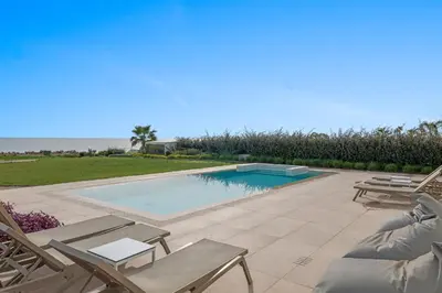 a swimming pool with chaise lounges and chairs and the ocean at Serenity Waves Villa 5 in Larnaka