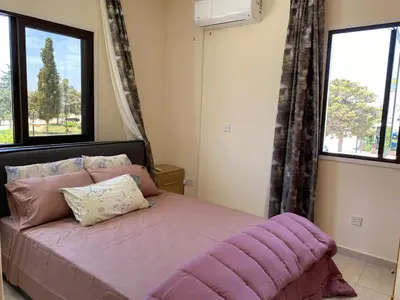a bedroom with a bed with a purple comforter and two windows at A sea breeze house in Voroklini