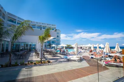 a resort with a pool with people laying on chairs and umbrellas at Evalena Beach Hotel in Protaras
