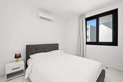 a white bedroom with a bed and a window at Maestro City Apartments in Larnaka