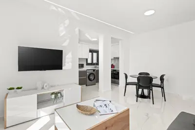 a white living room with a tv and a table at Maestro City Apartments in Larnaka