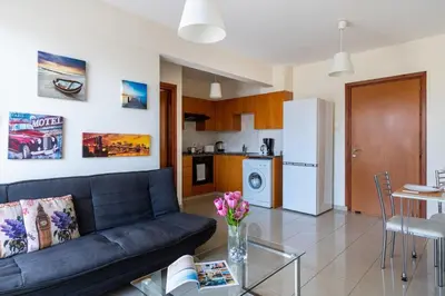 a living room with a black couch and a kitchen at Glade - 1 Bedroom Apt W Balcony in Larnaca in Larnaka