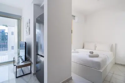 a white bedroom with a bed and a tv at Marble - Cozy Studio W Balcony in Larnaca in Larnaka