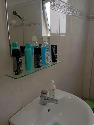a bathroom sink with a mirror and bottles on a shelf at Eat well Sleep Well in Larnaka