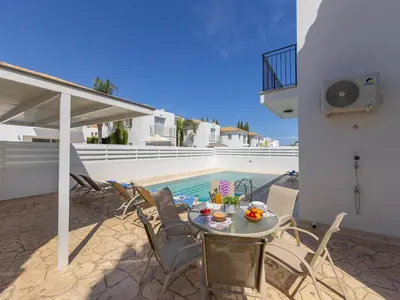 a patio with a table and chairs next to a pool at villa Sama palms 21 in Protaras