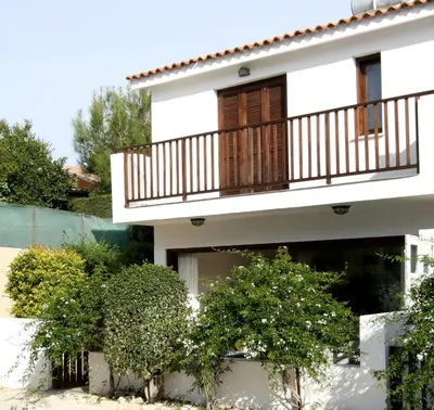 a white house with a balcony and some bushes at The Bay Villa in Pissouri
