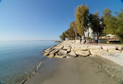 a beach with people sitting on a bench next to the water at Beach Walk - Central, Cool, Cute, Convenient in Limassol