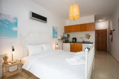 a bedroom with a white bed and a kitchen at Palmove Makenzy Ria Studio in Larnaka