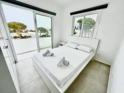 a white bed in a room with large windows at Protaras Cozy2bedroom Apartment in Paralimni