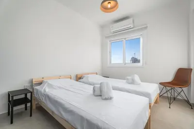 two beds in a room with a window and a chair at Modern seaview apartment in the heart of Agia Napa in Ayia Napa