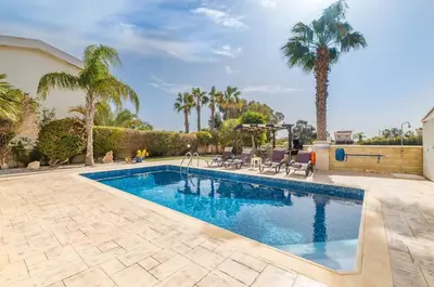 a swimming pool with chairs and palm trees at Tranquility Villa in Ayia Napa