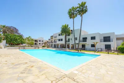 a swimming pool in front of a building with palm trees at Cozy Apartment in Kapparis # 506 in Paralimni