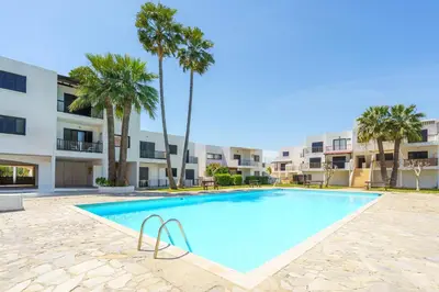 a swimming pool with palm trees in front of a building at Cozy Apartment in Kapparis #80 in Paralimni