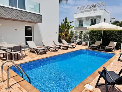 a swimming pool with chairs and an umbrella next to a house at Nissini Wana Luxury Villa in Ayia Napa
