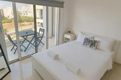 a bedroom with a white bed and a balcony with a table at White Sea View Apartment in Limassol