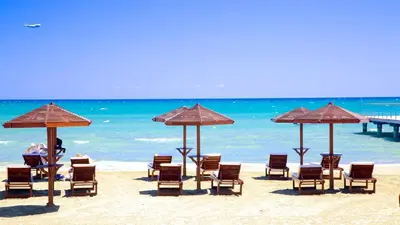 a group of chairs and umbrellas on a beach at Spacious Larnaca Beach Apartment in Larnaka