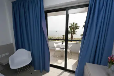 a room with blue curtains and a view of the ocean at Finikoudes Sunrise Sea View Lux in Larnaka