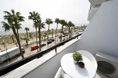 a balcony with a white table and palm trees at Finikoudes Sunrise Sea View Lux in Larnaka