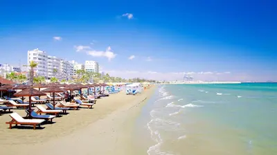 a beach with chairs and umbrellas and the ocean at Modern Larnaca Beach Apartment in Larnaka