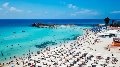 a crowd of people on a beach with umbrellas at Cornelia Hotel Ayia Napa Center in Ayia Napa
