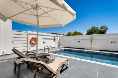 a patio with an umbrella and chairs next to a swimming pool at PANATHEON - Luxury 1 & 2 bdr bungalows 300 meters from sandy beach! in Ayia Napa
