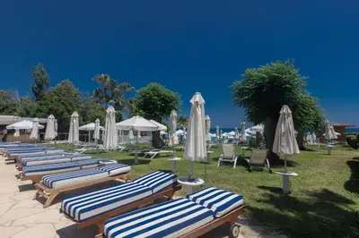 a row of chaise lounges with umbrellas and chairs at Iliada Beach Hotel in Protaras