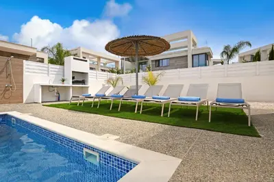 a pool with chairs and an umbrella next to a building at Villa Violeta - 3bed Bungalow large pool in Protaras