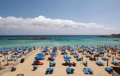 a beach with chairs and blue umbrellas and the ocean at Silver Sands Beach Hotel in Protaras