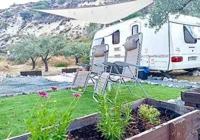 an rv parked in a yard with chairs and flowers at Olive Grove Mountain Caravan in Limnatis