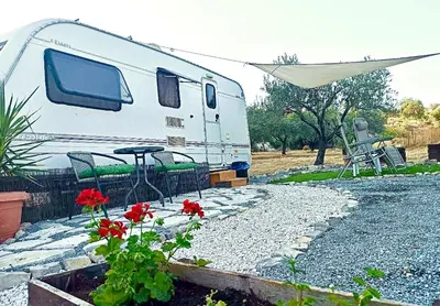 a white rv parked next to a patio with red flowers at Olive Grove Mountain Caravan in Limnatis