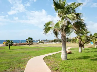 a path in a park with palm trees and the ocean at Nelia Sea Breeze in Ayia Napa