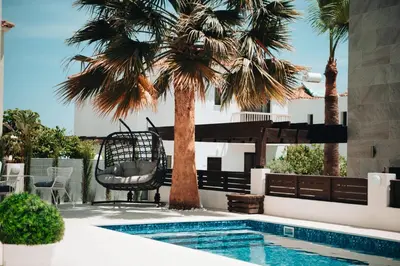 a swimming pool with a palm tree next to a house at Villa Lela in Paralimni