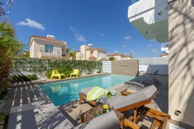 a swimming pool with chairs and a house at Protaras El Sol Villa in Protaras
