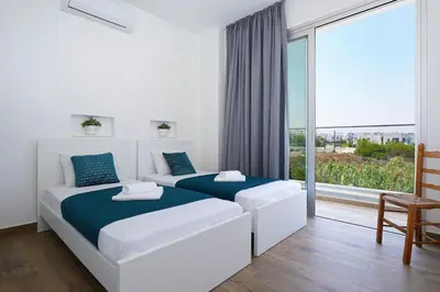 a white bedroom with two beds and a large window at MAREN - 250m from Golden Sandy Beach in Paralimni